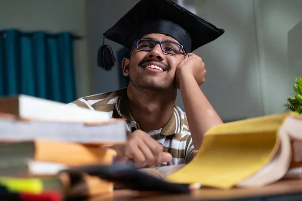 Young student dreaming about graduation while studing book or preparing for examination at home - concept of daydreaming and future career goal and education. — Stockfoto