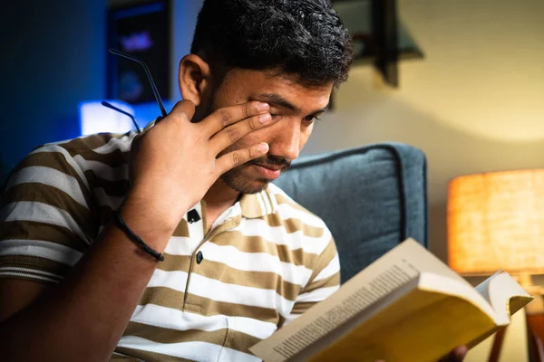 Primer plano disparó joven estudiante con gafas frotando los ojos debido a la tensión de los ojos al leer el libro durante la noche concepto de sentirse cansado, estudio temprano en la mañana y la educación — Foto de Stock