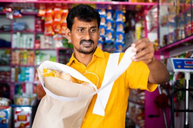 Shocked customer at Kirana or grocery store after seeing groceries bill receipt - concept of inflation, increasing in prices and consumerism.