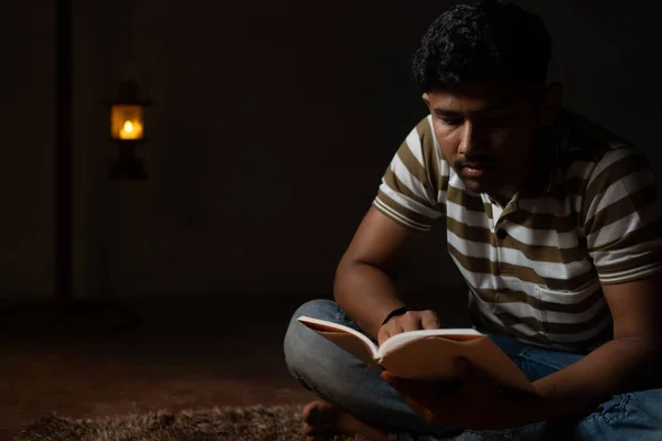 Young student busy reading during night under oil lamp or lantern due to power loss and Poverty - concpet of power cut, blackout during examination. — Photo
