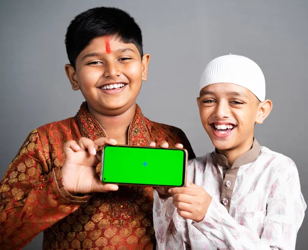 Ευτυχισμένα χαμογελαστά πολυεθνικά Ινδικά θρησκευτικά παιδιά κρατώντας κινητό με πράσινη οθόνη σε γκρι φόντο - conpet της διαφήμισης εφαρμογής προώθηση, τη φιλία και την ενότητα στην πολυμορφία. — Φωτογραφία Αρχείου