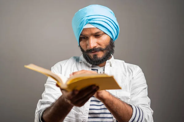 Jeune homme sikh lisant les Saintes Écritures religieuses pour prier Dieu sur fond gris - concept de croyants spirituels, culte et culture traditionnelle. — Photo