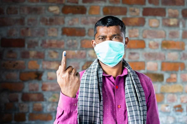 Bouwvakker met medisch gezichtsmasker met inkt gemarkeerde vinger na de verkiezingen door te kijken camera - concept van democratie en Indiase poll systeem — Stockfoto