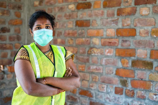 Magabiztos nő építőipari alkalmazott orvosi arc maszk és biztonsági kabát áll a kamera keresztbe karok a munkahelyen - koncepció vissza dolgozni során coronavirus covid-19 járvány — Stock Fotó
