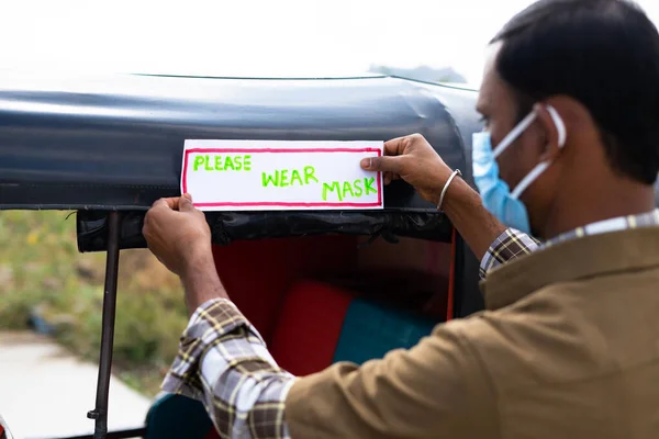 Céntrate en el aviso, Conductor automático con pegado de mascarillas médicas Por favor, use el signo de máscara boarb en Auto rickshaw como medida de seguridad coronavirus covid-19 y para proteger a los transeúntes de la infección viral —  Fotos de Stock