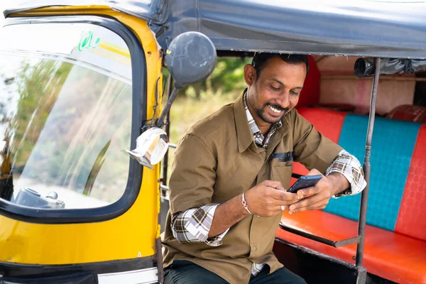 Joven indio rikshaw auto o taxista ocupado con el teléfono móvil mientras está sentado en el auto - concepto de tomar un descanso, el uso de las redes sociales en el teléfono inteligente y la tecnología. —  Fotos de Stock