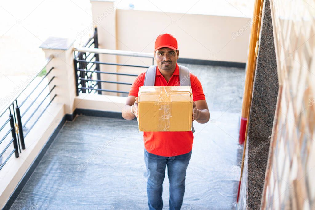 focus on box, Delivery boy placing parcel in front of door after showing parcel to cctv or security camera - concept of security, safety and home courier service