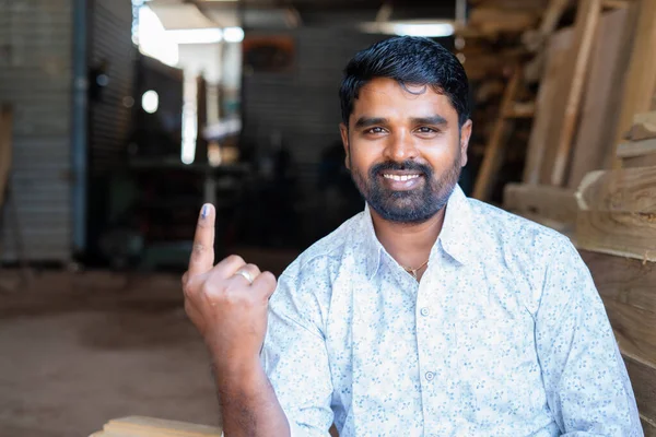 Happy indian carpainter or craftman showing ink marked finger by looking at camera after voting on election - concept of people voting rights, democracy and happiness