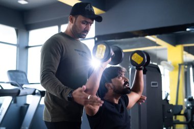 Müşteri, spor eğitmeni spor yaparken dambıl kullanmasına yardım eden spor eğitmeni - fitness eğitimi konsepti, kişisel antrenör ve vücut geliştirme.