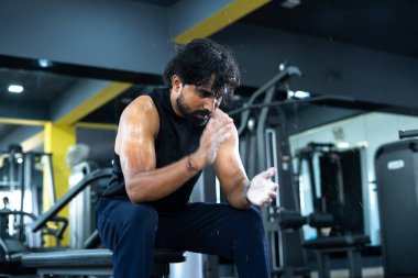 Genç terli Hintli vücut geliştirici spor salonunda toza el çırpıyor - sıkı çalışma konsepti, sağlıklı yaşam tarzı, vücut uygunluğu ve motivasyon veya ilham