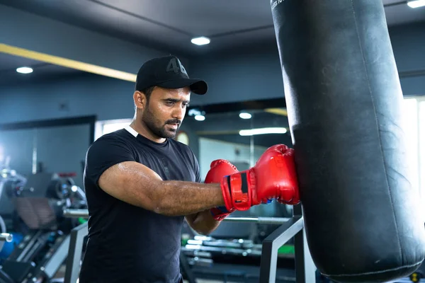 Mladý indický boxer bít boxovací pytel s rukavicemi v tělocvičně - koncept hubnutí, péče o tělo a fitness. — Stock fotografie
