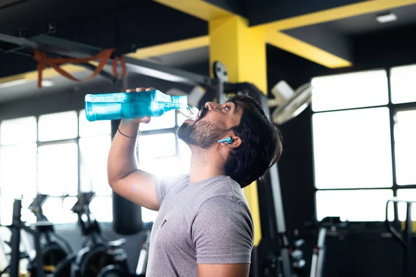 Žíznivý mladý indický svalař pitná voda po cvičení v tělocvičně - koncept relaxace, zdravého životního stylu a tvrdého cvičení nebo fitness tréninku. — Stock fotografie