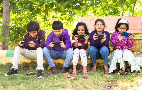 Bir grup çocuk parkta otururken cep telefonu kullanmakla meşgul- akıllı telefon bağımlılığı, video oyunu oynamak, teknolojinin fiziksel aktivitesini ve etkisini azaltmak,