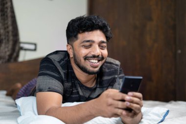 Mutlu gülümseyen genç adam geceleri yatakta mobie telefon kullanmakla meşgul. Flört uygulaması, sosyal medya ve online sohbet kavramı.