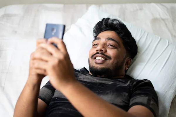 Heureux jeune homme bavarder sur le téléphone mobile tout en dormant sur le lit concept d'utilisation des médias sociaux, sortir ensemble app, flirter et la technologie. — Photo