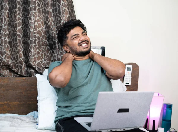 Mladý muž trpící bolestí šíje a zad při používání notebooku na posteli při práci z domova - koncepce nevhodného pracovního držení těla, přepracované a vyčerpané — Stock fotografie