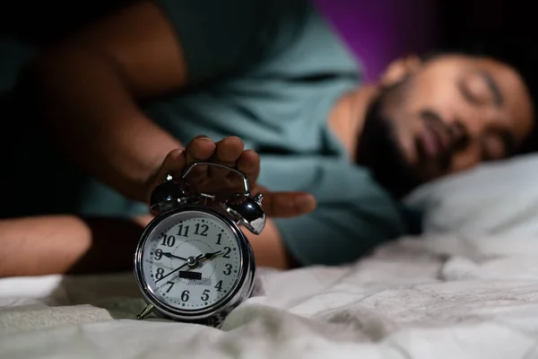 Focus on alarm, young man waking up early morning by turning off alarm - concept of active healthy lifestyle and morning routine. — Stock Photo, Image