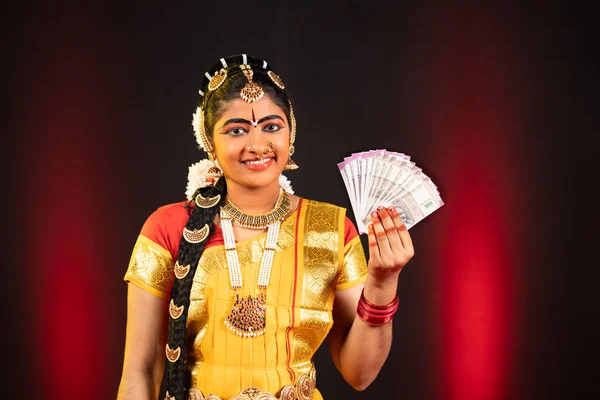 Danseuse indienne souriante Bharatanatyam tenant des billets de monnaie en regardant la caméra - concept de gains, de finances et de services bancaires. — Photo
