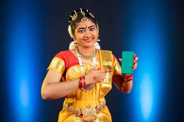 Indiase bharatanatyam danser tonen groene scherm mobiele telefoon door met de vinger te wijzen terwijl het kijken naar de camera - concept van app reclame, promotie en kunstenaar. — Stockfoto