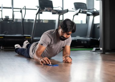 Spor salonunda cep telefonuna zamanlayıcı koyarak şınav çeken genç bir adam. Kas ya da vücut geliştirme, kalori izleme ve teknoloji kavramı..