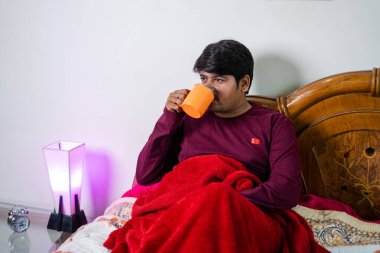 Genç adam sabahları yatak odasında oturarak kötü kahve içiyor - günlük rutin konsept, ferahlatıcı ve kişisel bakım.