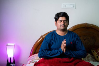 Genç adam uyumadan önce yatağa ellerini katlayarak Tanrı 'ya dua ediyor. Manevi inanç, sağlıklı uyku ve tefekkür kavramı.