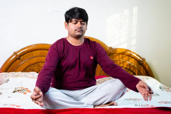 Jonge indiaanse man doet meditatie met de ogen dicht op bed- concept van een gezonde levensstijl, mindfulness en streelt verlichting — Stockfoto