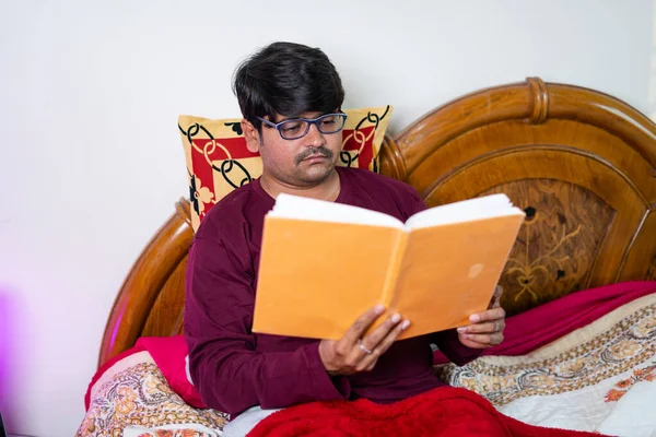 Jeune homme avec des lunettes livre de lecture avant de dormir dans la chambre - concept de passe-temps, de bien-être et de routine nocturne — Photo