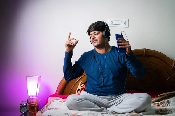 Profiter du chant du jeune homme en écoutant des chansons sur téléphone portable avec casque dans la chambre concept de divertissement, de détente et d'autosoin. — Photo