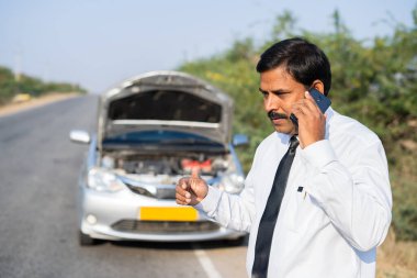 Otoyoldaki araba arızası, mobil araba tamiri, yardım ve iletişim kavramı hakkında endişeli bir işadamı, araba tamircisiyle konuşurken cep telefonuyla konuşuyor.