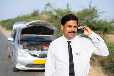 Otoyoldaki araba arızası, iletişim konsepti, araba onarım ve rahatlama gibi konularda araba tamircisiyle telefonda konuşan bir iş adamı..