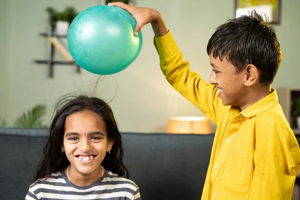 Focus on boy, Kids enjoys static cling experiment by playing while rubbing ballon to hair and hairs attracted to ballon - conept of excitement and home science experiment. — Stock Photo, Image
