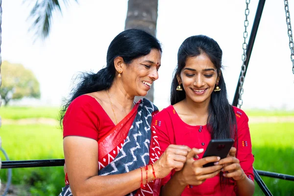 Розслаблені мати і дочка на гойдалці за допомогою мобільного телефону - поняття щастя, зв "язку, використання соціальних медіа та індійської сім" ї — стокове фото
