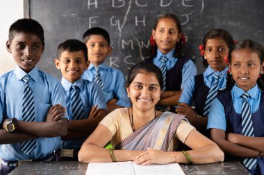 Siyah kurul önünde sınıfa kamerayla bakan öğrencili mutlu öğretmen - destek, eğitim, büyüme, istihdam ve iş kavramı.