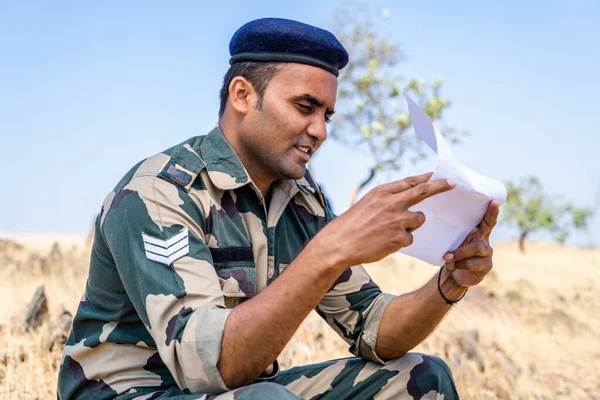Joven soldado indio leyendo carta o correo de un miembro de la familia mientras está al servicio en la cima de Mountian - concepto de familia desaparecida, vinculación y comunicación a distancia — Foto de Stock