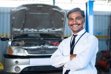 Otomobil garajında kendine güvenen bir yönetici ya da yönetici kameraya bakarak çapraz kollarla ayakta duruyor. Başarılı mesleğin, kariyerin ve iş adamlarının birleşimi.