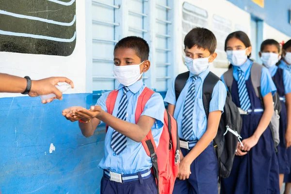 Los niños en edad escolar con mascarilla médica se someten a pruebas de temperatura y aplicación de desinfectante antes de entrar en clase - concepto de coronavirus covid-19 precauciones, medidas de atención médica y volver a la escuela. —  Fotos de Stock