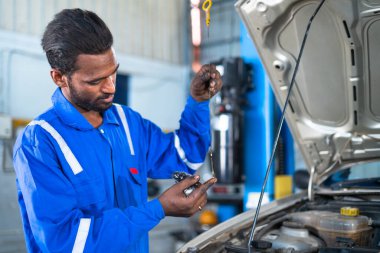 Otomobil tamircisi motor yağı seviyesini garajda kaput açarak inceliyor - bakım hizmeti kavramı, mavi yaka işleri ve kayganlaştırıcı denetimi.