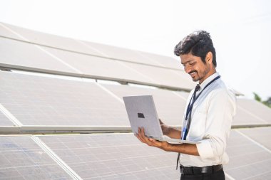 gülümseyen mühendis tarla arazisindeki güneş paneli önünde çalışarak işlemleri kontrol ediyor - teknoloji kavramı, sürdürülebilir yaşam tarzı ve profesyonel işgal.