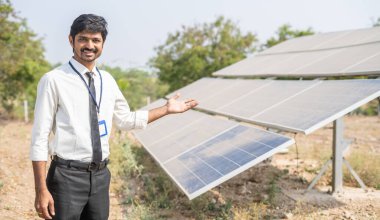 Tarım arazisindeki güneş enerjisi panellerini gösteren mutlu gülümseyen mühendis - yenilenebilir enerji, sürdürülebilir yaşam tarzı ve yatırım ve bankacılık için destek kavramı