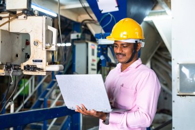 Üniformalı mühendis fabrikadaki makinelerde dizüstü bilgisayarda çalışmakla meşgul - teknoloji, kalifiye veya profesyonel iş gücü ve geliştirme kavramı.