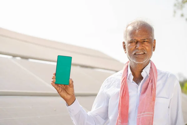 Tarım arazisinde güneş panelinin önünde dikilirken yeşil ekran cep telefonu gösteren gülümseyen çiftçi - uygulama reklamı kavramı, sürdürülebilir enerji tanıtımı — Stok fotoğraf