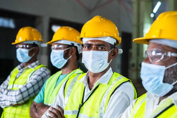 Grupp av fabriksarbetare med ansiktsmask, glasögon och hatt tittar på kameran genom - begreppet arbetarskyddsåtgärder och skydd mot coronavirus eller covid-19 infektion — Stockfoto