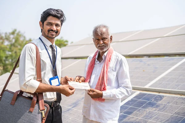 Köy çiftçisi güneş paneli önünde bankacıdan çek alıyor - yenilenebilir enerji üretimi, tarım kredisi ve borcu için finansal destek kavramı. — Stok fotoğraf