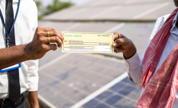 Çiftçinin güneş paneli önünde bankacıdan çek aldığı yakın çekim - yenilenebilir enerji üretimi, tarım kredisi ve borç için finansal destek kavramı. — Stok fotoğraf