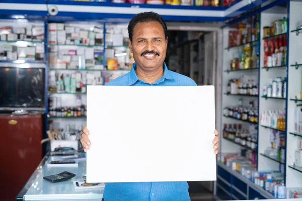 Retrato de un empleado médico sonriente mostrando letreros blancos vacíos mirando a la cámara en la farmacia minorista: concepto de promoción, farmacéutico y publicidad — Foto de Stock