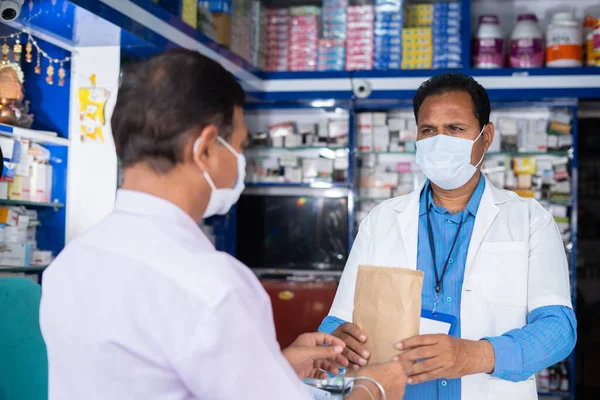Vásárlók gyógyszereket vásárolnak a gyógyszerésztől, miközben mind az orvosi maszk a kiskereskedelmi üzletben a covid-19 koronavírus világjárvány idején - az egészségügyi, orvosi és biztonsági intézkedések fogalma. — Stock Fotó