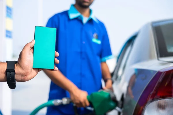 close up shot of hand showing green screen mobile phone while worker filling petrol on car - concept of application advertisement, promotion and offers.