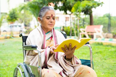 Yaşlı engelli kadın parkta tekerlekli sandalyede otururken kitap okuyor - rahatlama, ferahlama ve bilgelik kavramı.