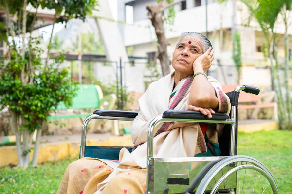 Pensamento profundo mulher idosa deficiente em cadeira de rodas no parque - conceito de depressão, solidão e cuidados de saúde — Fotografia de Stock
